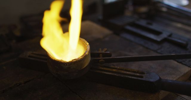 Molten metal in a heated crucible held by tongs suggesting blacksmithing or metalworking process. This is perfect for illustrating concepts of industrial work, craftsmanship, and heat-related processes. Ideal for use in articles, advertisements, or educational materials about metalworking, traditional manufacturing skills, and industrial processes.