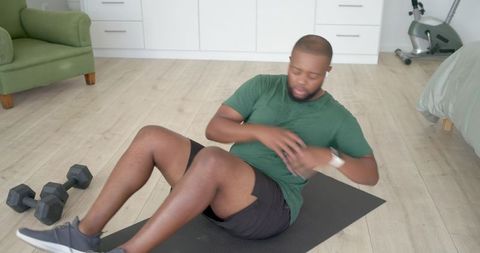 Home core workout man doing russian twists on mat with dumbbells and smartwatch