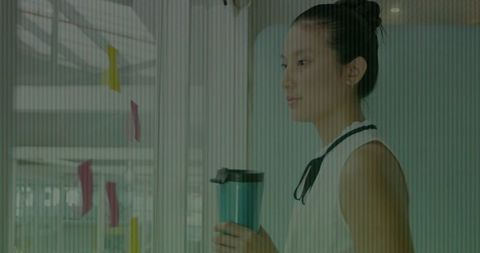 Businesswoman holding mug gazing at sticky notes on glass wall