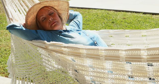 Senior woman comfortably relaxing in hammock, wearing sun hat. Ideal for leisure, outdoors relaxation, aging gracefully, and stress relief concepts.