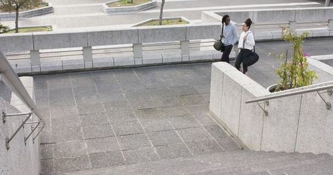Diverse friends walking with duffel bags on urban elevated plaza, casual conversation
