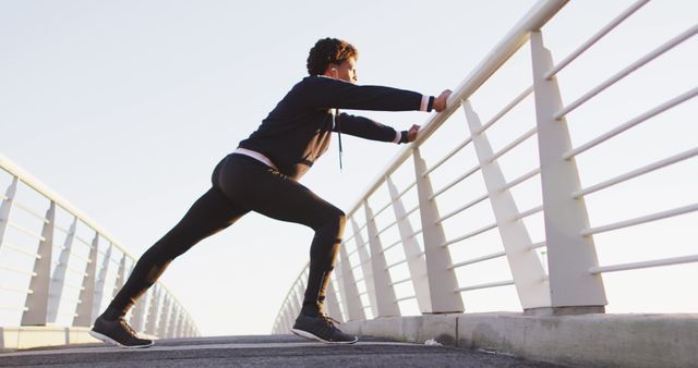 Woman stretching muscles on an urban bridge during morning light. Perfect for advertising healthy lifestyle, fitness training, morning workout routines, urban fitness trails, and exercising outdoors.