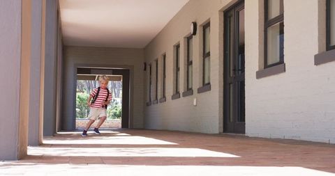 Young boy walking along sunlit school corridor with backpack and room for text or copy
