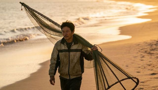 Lone asian fisherman carrying conical net on golden beach at sunset