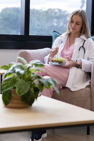 Female doctor eating healthy takeout salad during rainy break in clinic lounge area
