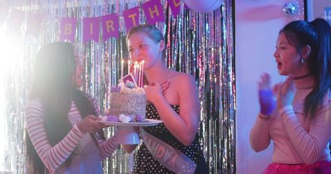 Teen friends celebrating birthday with sparkly tinsel backdrop, polka dot dress and cake