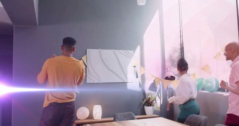 Coworkers decorating modern office breakroom with pastel bunting, balloons and sunlit art