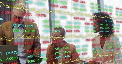 Multigenerational team analyzing stock market tickers through glass partition in boardroom