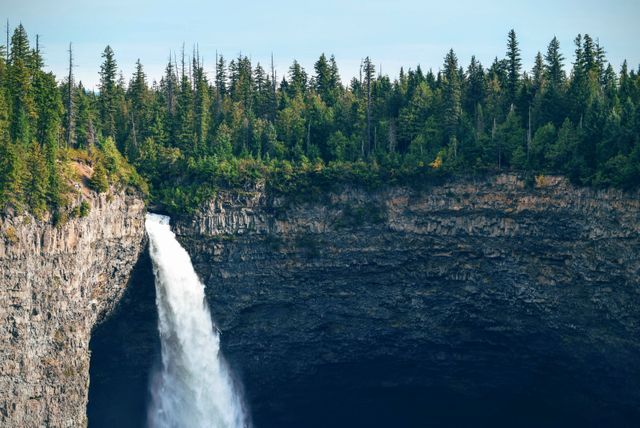 This image showcases a breathtaking waterfall plunging over a steep cliff into a lush forested canyon, surrounded by dense, green trees. Perfect for tourism brochures, nature magazines, travel websites, and outdoor adventure promotions focusing on beautiful natural landscapes.
