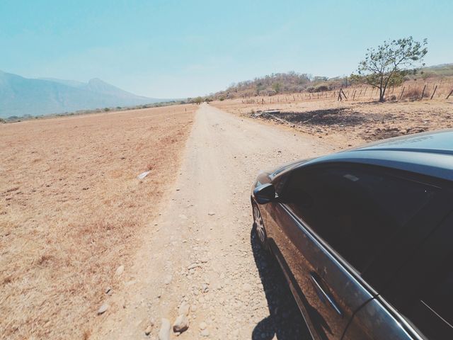 Car cruising along a lonely dirt road in a dry, rural area on a clear day. Ideal for topics about road trips, adventures, travel destinations, remote places, and nature exploration.