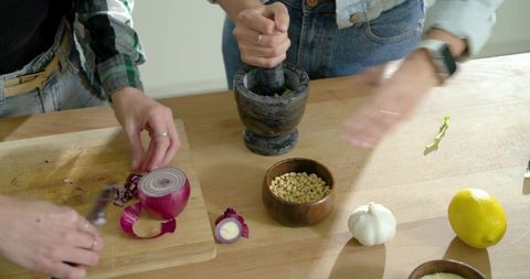 Diverse friends chopping red onion and pressing herbs with mortar on wooden counter