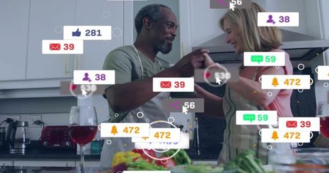 Mature couple holding hands while preparing salad in modern kitchen with social notifications