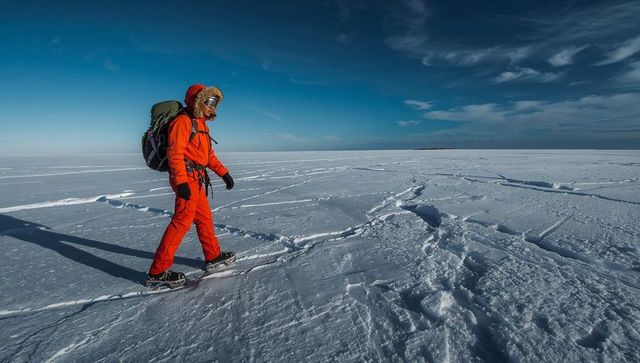 Walking explorer in bright orange parka crossing vast polar ice with snowshoes and pack
