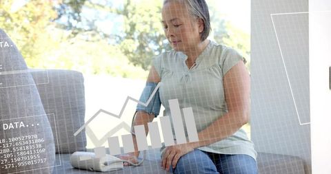 Senior woman measuring blood pressure at home with digital monitor and health data overlay