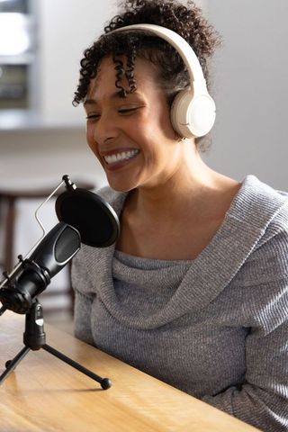 African american woman recording podcast at home studio smiling into pop-filter microphone