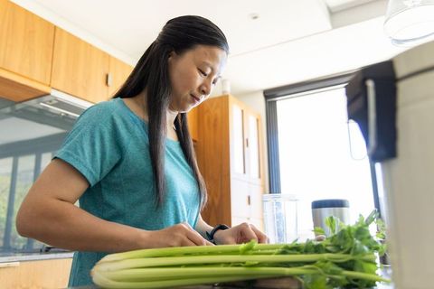 Mature asian woman chopping celery on kitchen counter preparing healthy smoothie ingredients