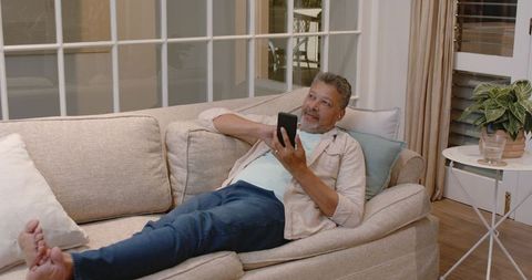 Senior Man Relaxing on Couch Using Smartphone at Home