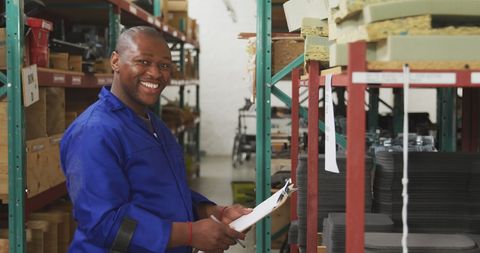 Warehouse worker on crutches smiling and writing on clipboard