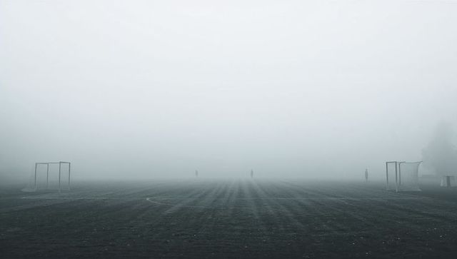 Misty soccer field with distant silhouettes and goal frames evoking solitude and minimalism