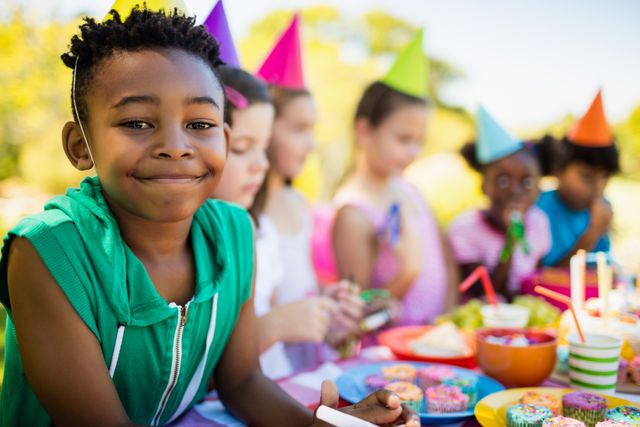 Close up of cute boy smiling in front of other children during a birthday party on a park 