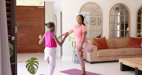 Mother and teenager practicing yoga on purple mats in modern living room for family wellness