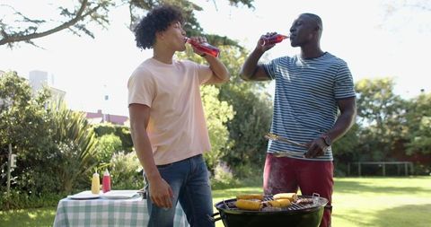 Friends grilling and enjoying soda in sunny backyard setting