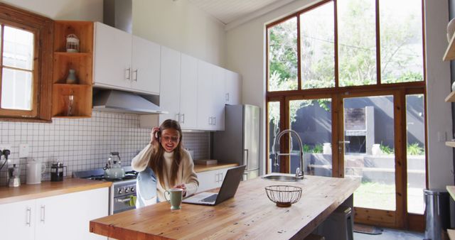 Young woman enjoying coffee while working on laptop in modern kitchen - Download Free Stock Images Pikwizard.com