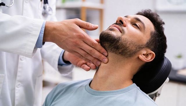 Doctor palpating patient neck during thyroid exam, reclining male patient in clinic