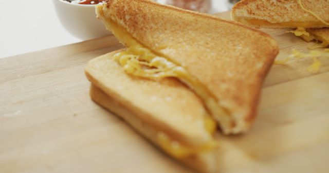 Close-up of a warm grilled cheese sandwich with gooey melted cheese oozing from between the perfectly toasted slices of bread, placed on a wooden surface. Ideal for food blogs, culinary websites, cooking tutorials, or marketing for cafes and restaurants promoting breakfast or snack options.