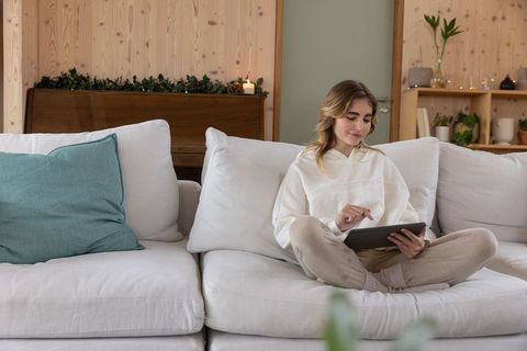 Woman Relaxing on Sofa with Tablet in Cozy Candlelit Living Room