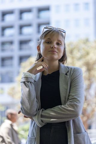 Confident young female professional standing in city, touching chin, wearing light gray blazer