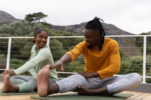 Multicultural couple stretching and smiling on outdoor deck yoga mats with mountain view