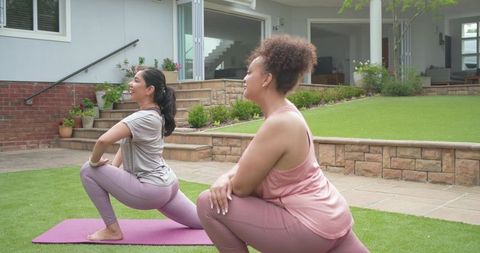 Diverse women stretching and warming up in backyard garden doing lunges on purple yoga mat
