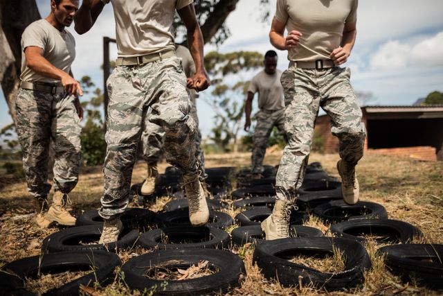 Military soldiers are undergoing rigorous training at a boot camp, navigating an obstacle course made of tires. This image can be used for articles or advertisements related to military training, physical fitness programs, teamwork exercises, or recruitment campaigns.