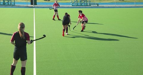 Teenage female field hockey players contesting ball on bright green turf during match