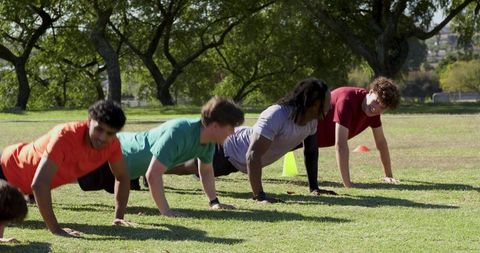 Diverse male team doing push-ups on grass field celebrating high-fives after workout