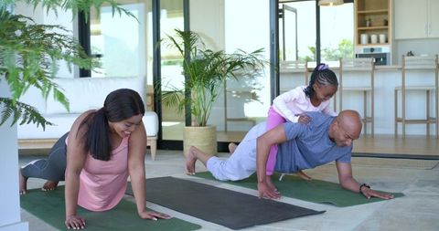 Active family doing plank workout at home, daughter climbing on father's back