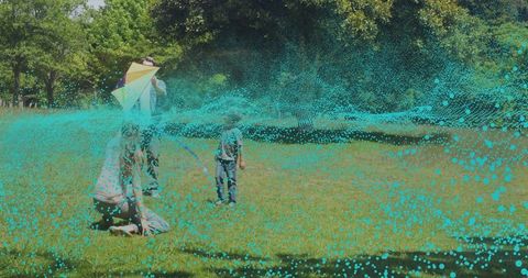 Family flying kite in sunlit park with teal particle wave overlay for technology concept
