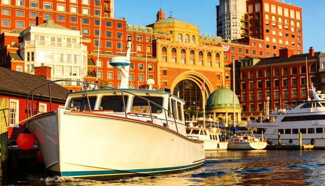 Gliding white cabin cruiser at sunlit urban harbor with historic arched waterfront buildings
