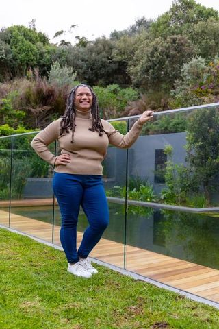 African american woman smiling and leaning on glass railing by backyard pond and deck
