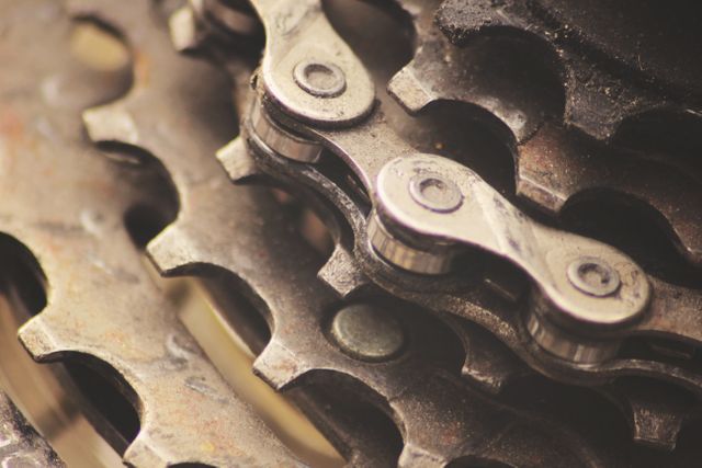 Close-up view of a bicycle chain and gear mechanism, featuring intricate details of metal links and sprockets. Useful for themes related to cycling, bike maintenance, engineering, and machinery. Perfect for illustrating concepts of technology, motion, and industrial design.