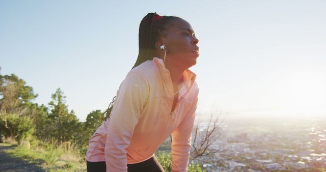African american woman exercising outdoors wearing earphones preparing to run in countryside. healthy outdoor lifestyle fitness training.