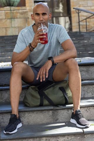 Fit african american man sitting on steps sipping refreshing drink with duffel bag, urban