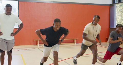 Coach guiding african american men performing lunges and sprint drills in indoor gym