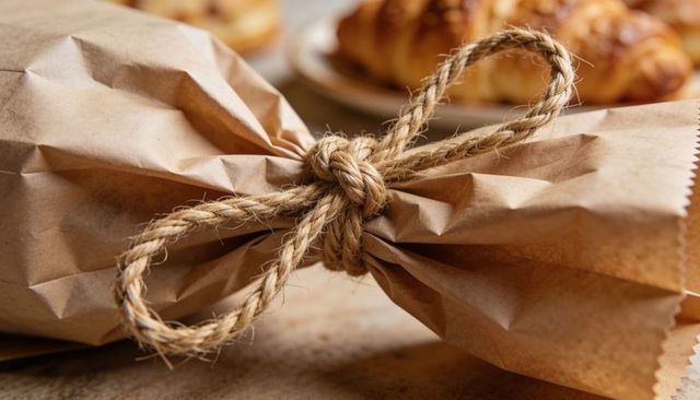 Rustic kraft paper package wrapped with jute twine bow on wooden bakery counter with croissants