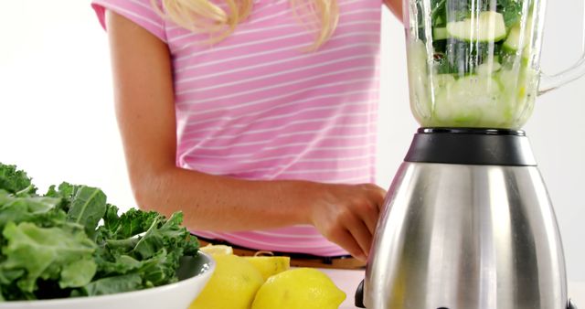 Ideal for use in articles, blogs, and advertisements promoting healthy living, nutrition, fresh diets, and smoothie recipes. Visual representation of making a nutritious green smoothie with kale, lemon, and fresh ingredients.