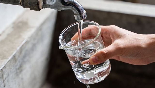 Pouring water into glass graduated beaker under faucet, measuring flow and volume