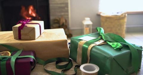 Wrapped gifts resting by cozy glowing fireplace with green ribbon, burlap, dried citrus