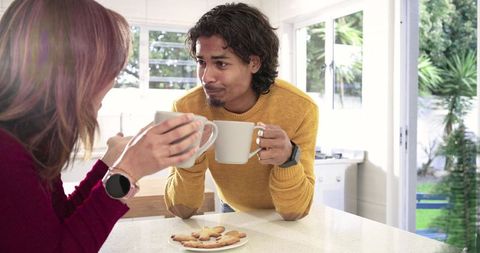 Couple sharing coffee and cookies at sunlit kitchen island, cozy morning conversation
