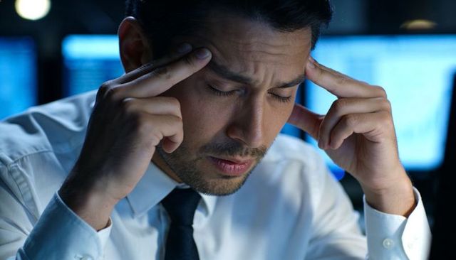 Stressed executive pressing temples during night shift amid glowing computer monitors
